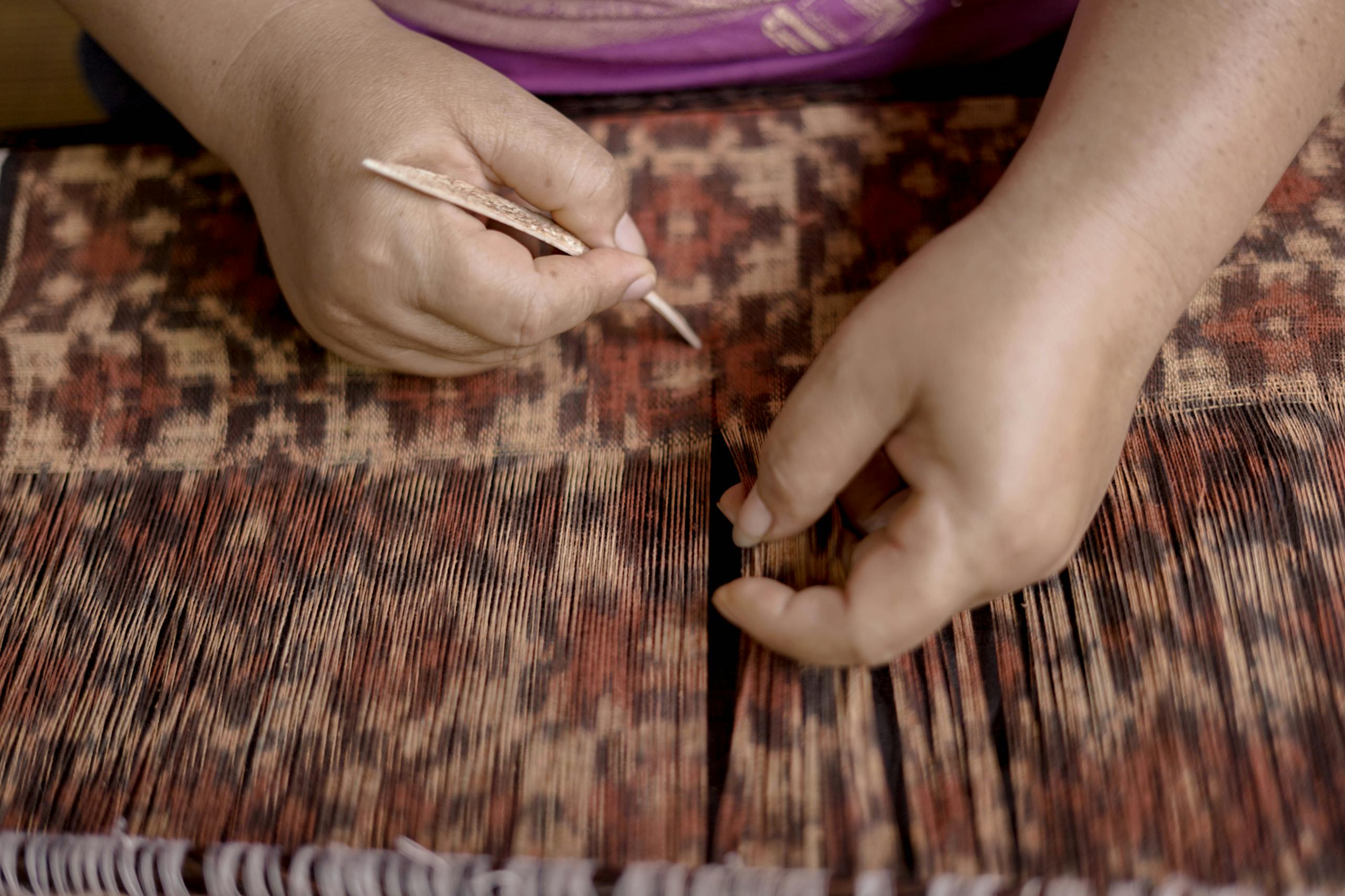 Close-up of hands weaving traditional Gringsing fabric in Tenganan, Bali, Indonesia.