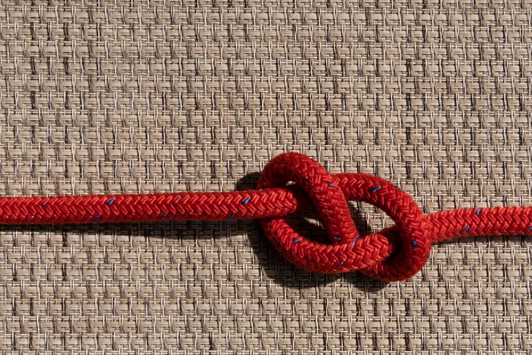 Detailed view of a red rope knot against a textured background.