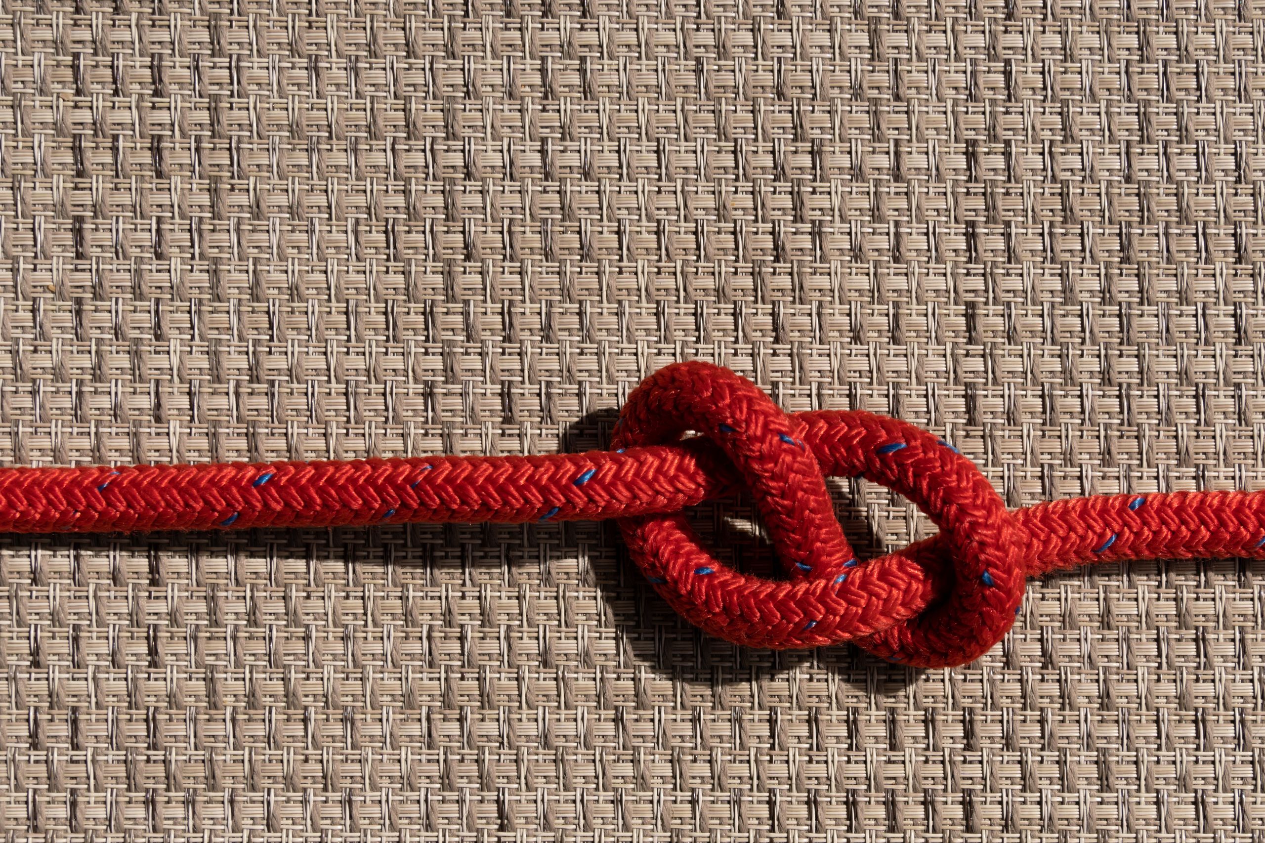Detailed view of a red rope knot against a textured background.